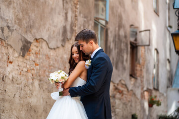 Beautiful young bride with wedding bouquet and groom near old castle before wedding ceremony