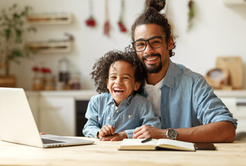 Happy african american family father and son sitting at table with laptop during distance education