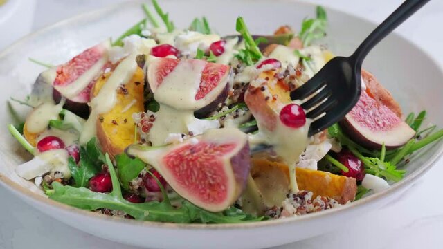 Eating warm autumn quinoa salad with baked vegetables, figs, feta cheese, pomegranate and dressing.