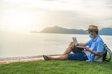 Man wear mask using laptop computer on beach  sea  and Man travel holiday Phuket sandbox Thailand are freedom life financial