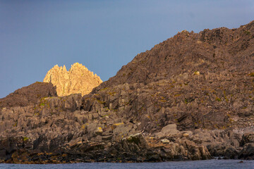 Fototapeta na wymiar Goldenes Abendlicht, das von der zerklüfteten Felswand an der Küstenlinie der Barentssee reflektiert wird