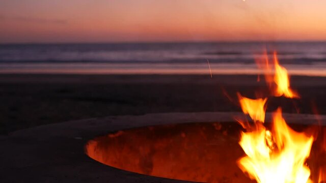 Campfire pit by Oceanside pier, California USA. Camp fire burning on ocean beach, bonfire flame in cement ring place for bbq, sea water waves. Romantic evening twilight sky, dusk after summer sunset.