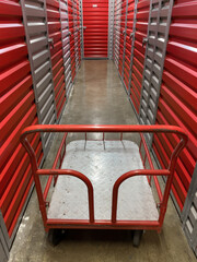 Storage corridor warehouse with cart . Self storage facility, red metal doors with locks. Moving, organizing, storage concept.selective focus