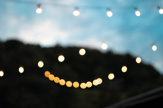 Light bulbs retro garland hanging in restaurant or cafe in the garden at evening time. Lighting decor. Bright blue sky with clouds