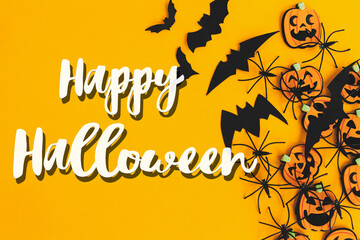 Happy Halloween text sign on pumpkins, jack o lanterns, spiders, bats border flat lay on orange background. Season's greeting card. Handwritten happy halloween text. Trick or treat
