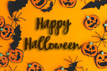 Happy Halloween text sign on pumpkins, jack o lanterns, spiders, bats frame flat lay on orange...