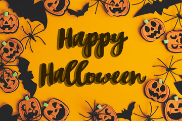 Happy Halloween text sign on pumpkins, jack o lanterns, spiders, bats frame flat lay on orange...