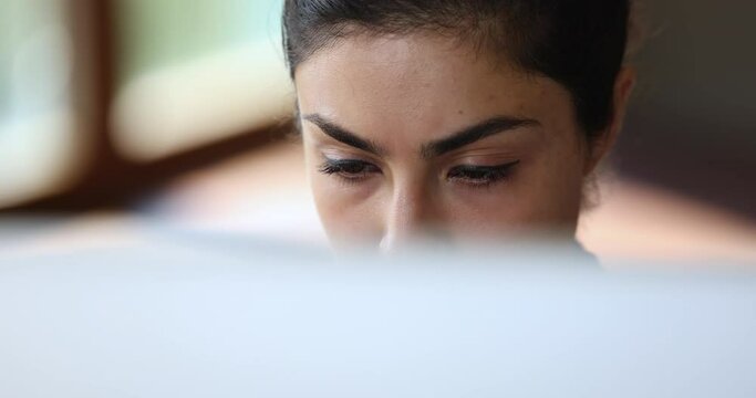 Close up face of focused young indian female looking on computer screen reading document online thinking on information doing remote job. Concentrated millennial woman practice distant work learning
