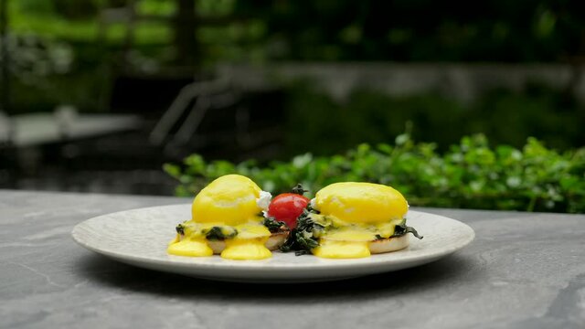 Healthy, nutritious breakfast. Fresh eggs Benedict on bun with green spinach and vegetables. Two poached eggs with yellow yolk sauce. Traditional English breakfast in a luxury hotel. Side view