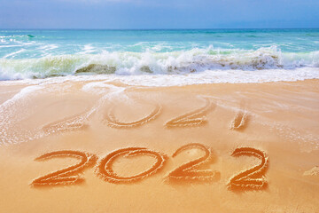 Fototapeta na wymiar 2022 written on the sand of a beach, ocean waves, travel new year greeting card