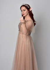 Full length  portrait of red haired  girl wearing a creamy fantasy gown and crystal crown, like a fairy goddess costume.  standing  pose with elegant gestural hands, isolated on  studio background