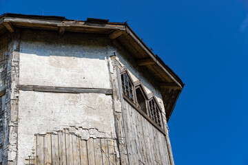 The upper part of an ancient watchtower made of stone blocks and wood paneling with windows against the blue sky on a bright sunny summer day. Close-up