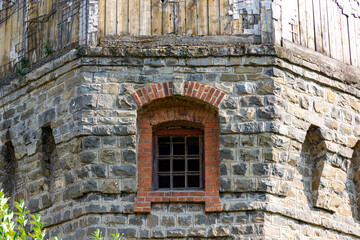 Red brick window of an ancient castle in a wall of natural gray stone. Arched construction. Summer sunny day. Close-up