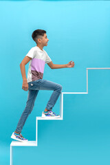 Young smiling teen boy climbs the development ladder against blue background. Education concept © rozaivn
