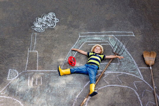 Adorable little kid boy playing with colorful chalks and painting big tractor picture on asphalt. Happy preschool child playing outside. Creative leisure for children outdoors in summer