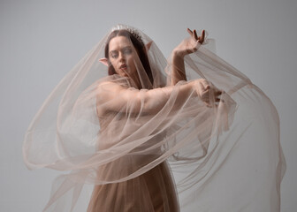 portrait of red haired  girl wearing a creamy fantasy gown and flowing veil fabric, like a fairy goddess costume.  standing  pose with elegant gestural hands, isolated on light studio background.