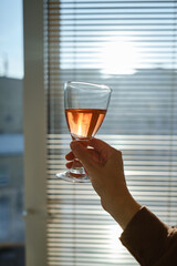 Glass of wine in the hands of a girl in the sun at home. Tasting of alcoholic beverages. Celebrate and enjoy the moment. Romantic evening aperitif. Glass of wine close up