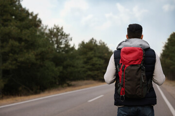 Man with backpack on road near forest, back view