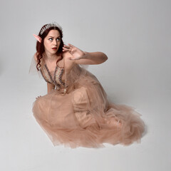 Full length  portrait of red haired  girl wearing a creamy fantasy gown and crystal crown, like a...
