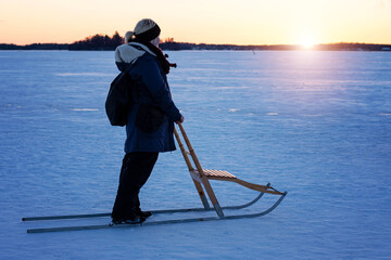 Woman with blonde hair in a ponytail in warm clothing on a wooden snow kick, also called kick sled,...