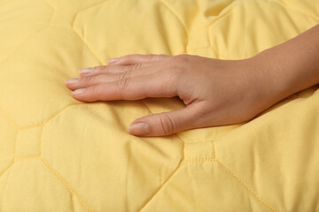 Woman touching soft yellow pillow, closeup of hand
