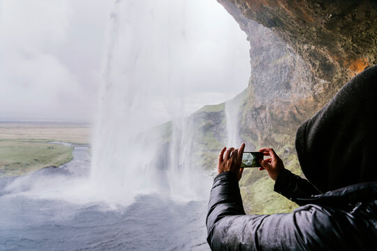 Anonymous tourist taking photo of amazing waterfall on smartphone on cloudy day