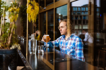 Pensive man drinking beer in bar in daylight