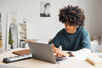 Portrait of male African-American student using laptop while doing homework in college dorm, copy...