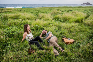 Musicians with guitar and ukulele lying on grass near sea in daylight