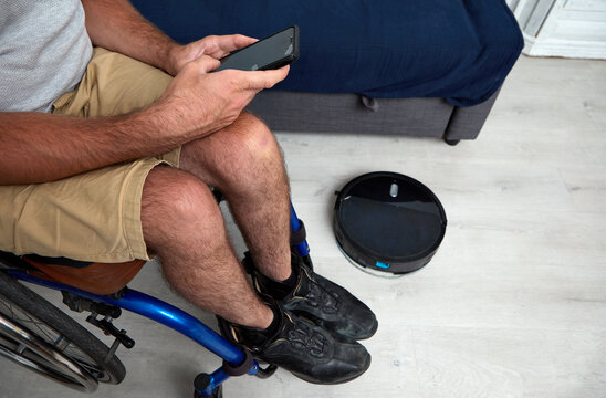 unrecognizable man in wheelchair controlling cleaning robot from smart phone