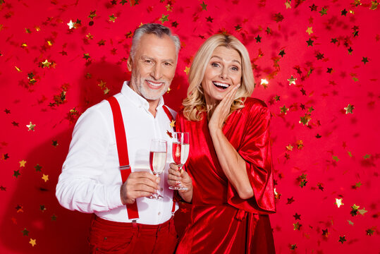 Photo of excited retired couple serpentine event champagne noel atmosphere isolated over red color background
