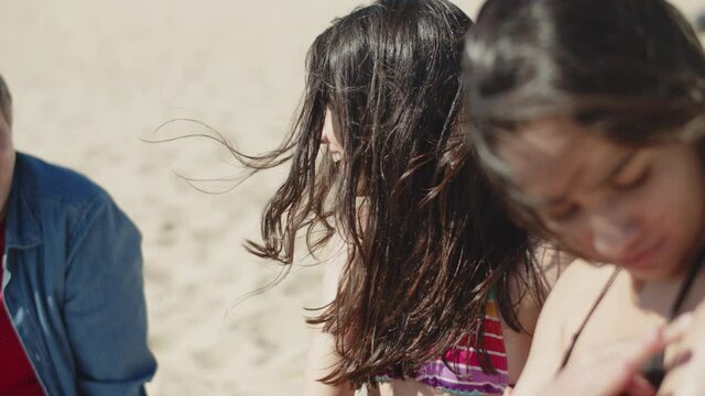 Side View Of Happy Kids Applying Sunblock Cream On Older Sister. Smiling Little Brother And Sister Sitting On Beach During Summer Vacation And Taking Care Of Elder Sisters Health. Family Concept