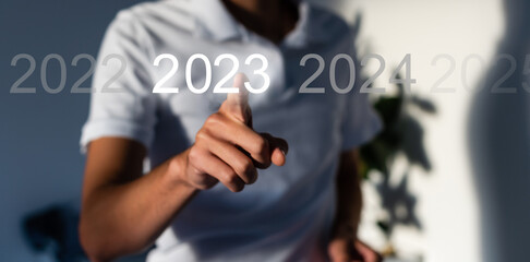 Finger pressing blue start 2023 button on virtual interface on gray background with copy space for text. Concept of new year. Businessman pressing 2023 start up business. Beginning of New Year 2023