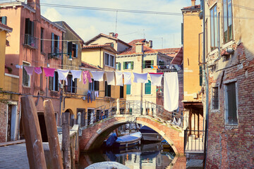 Fototapeta na wymiar Washing lines across canal in Venice, Italy. Laundry hanging on a clothes line between city buildings and above bridge. Clothes lines between windows of old brick houses in Venice.