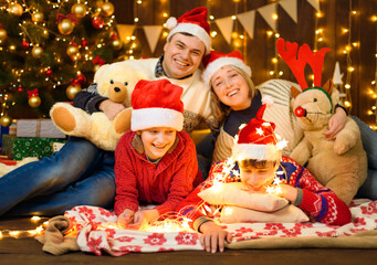 Fototapeta na wymiar Family posing in new year or christmas decoration. Portrait of children and parents. Holiday lights and gifts, Christmas tree decorated with toys.