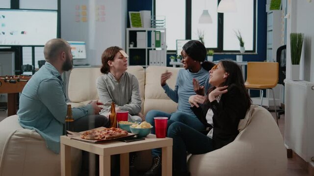 Cheerful coworkers playing guessing game with sticky notes on forehead after work for entertainment. Workmates enjoying fun activity with beer drinks, snacks and play after hours.