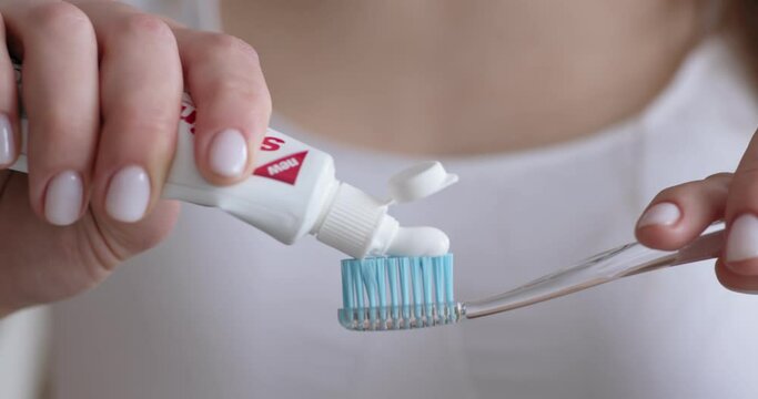 Woman squeezing toothpaste on toothbrush at home
