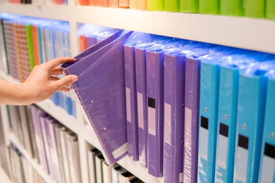 Male hand choosing new purple ring binder file folder from colourful shelf display in stationery shop. Buying office supplies concept