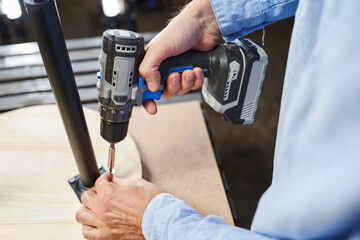 electric screwdriver in men's hands. tightening screws into legs on a wooden table