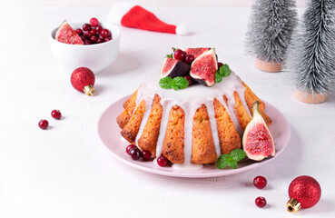 Christmas cake topped with icing, figs, cranberry and mint served on the plate. Dessert in festive table setting 