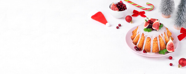 Web banner with Christmas cake topped with icing, figs, cranberry and mint on white table. Dessert in festive table setting. Template with copy space