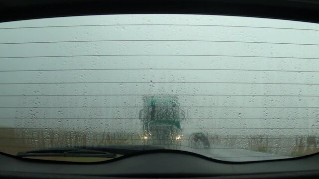Driving on the road in rain, view through the car rear windshield
