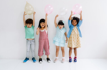 Group of adorable kids diverse cultures holding colorful balloons in party on the white wall...