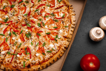 Pizza with pumpkin seeds and green onions in a cardboard box near mushrooms and tomatoes, close-up.