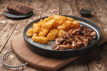 Fried potatoes with mushrooms on a wooden table near pieces of bread