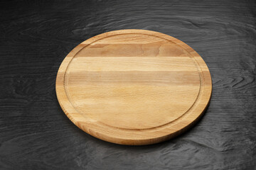 Wooden round board for serving dishes on a black background.