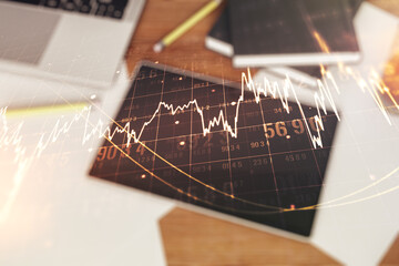 Multi exposure of abstract financial graph and modern digital tablet on desktop on background, top view, financial and trading concept