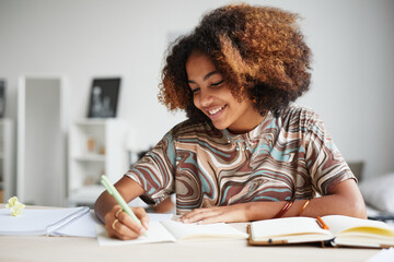 Front view portrait of female African-American student enjoying homework and smiling, copy space