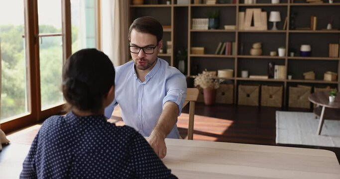 Friendly young male recruiter hr manager get up to welcome female applicant on vacant place with handshake before job interview. Smiling polite male employer meet lady job seeker start discuss resume