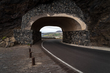 Fototapeta na wymiar Arch on the mountain road to Cape Teno. View from the observation deck - Mirador Punta del Fraile. In the background, the small town of Buenavista del Norte. Tenerife. Canary Islands. Spain.